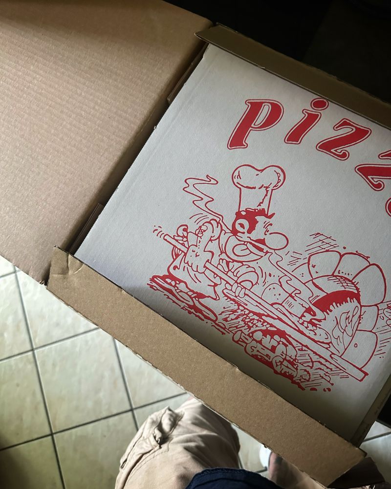 Ein frisch geöffnetes Paket, dessen Inhalt den Deckel eines Pizzakartons zeigt, welcher zur Stabilisierung und zum Schutz des Inhalts eingepackt wurde.